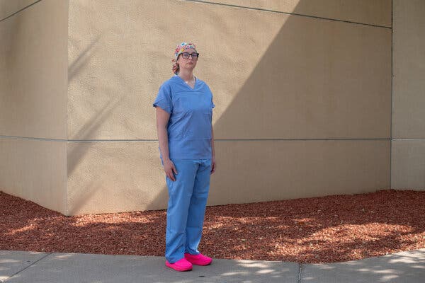 A women stands outside in blue medical scrubs, hot pink shoes and a colorful surgical cap.